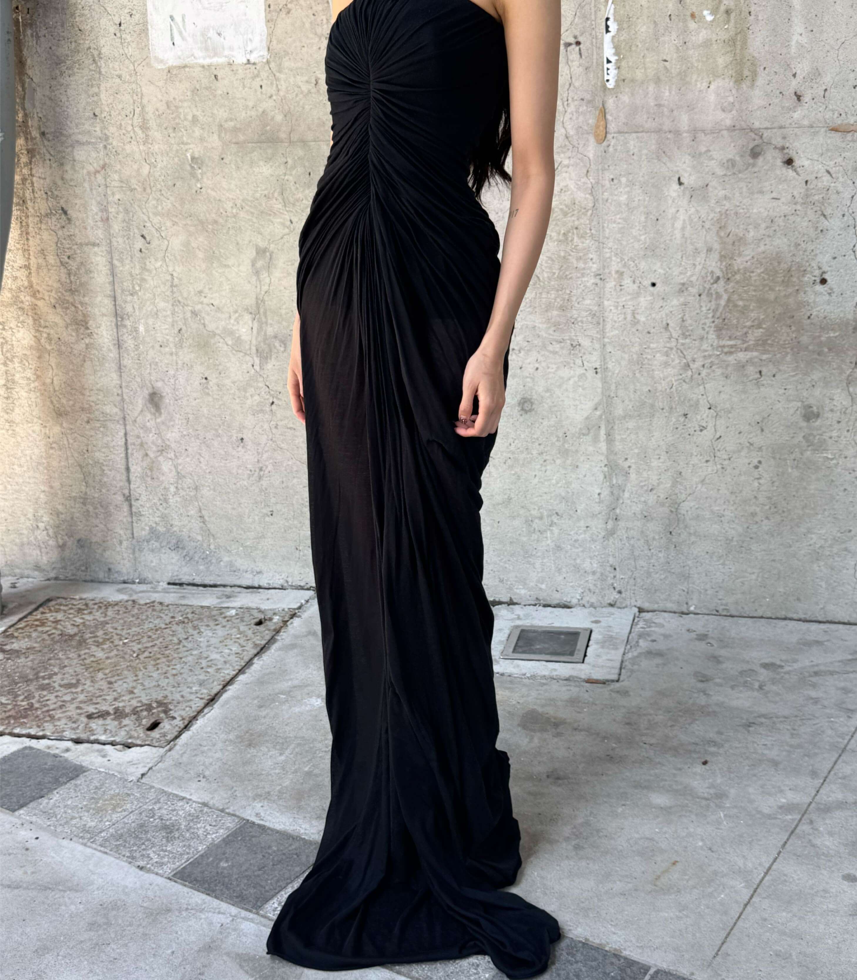 Rick Owens Black evening gown with a draped design worn by a person against a concrete wall.